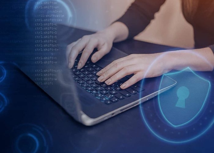 Experto en ciberseguridad trabajando en entorno digital Experto en ciberseguridad escribiendo código en una laptop con elementos gráficos de protección digital como escudos y candados.